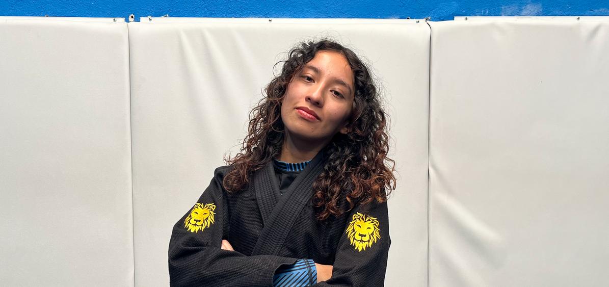 Karen guerra posando de brazos cruzados en atavío de Jiu Jitsu contra una pared acolchada blanca